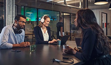 Bureau de travail vitr avec 3 individus assis autour d'une table et portant les casques audio EPOS sans fil