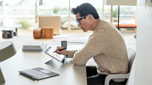 Homme avec les lunette sur son bureau travaillant sur une tablette microsoft
